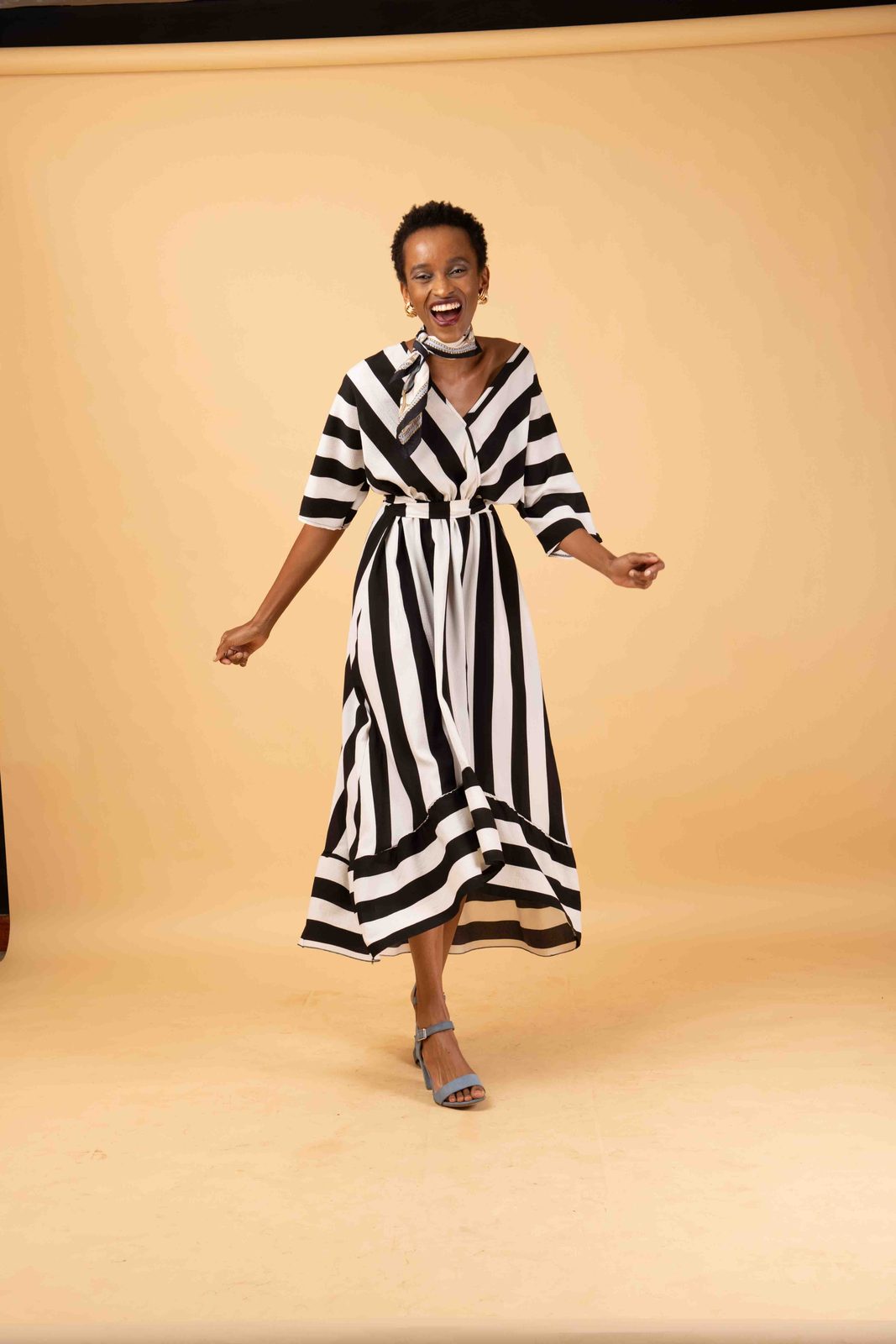 A model laughs in a black-and-white striped wrap dress with a flared hem against a cream studio backdrop.