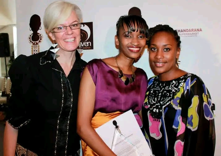 Three women at the awards event; the designer at centre holds an award certificate.