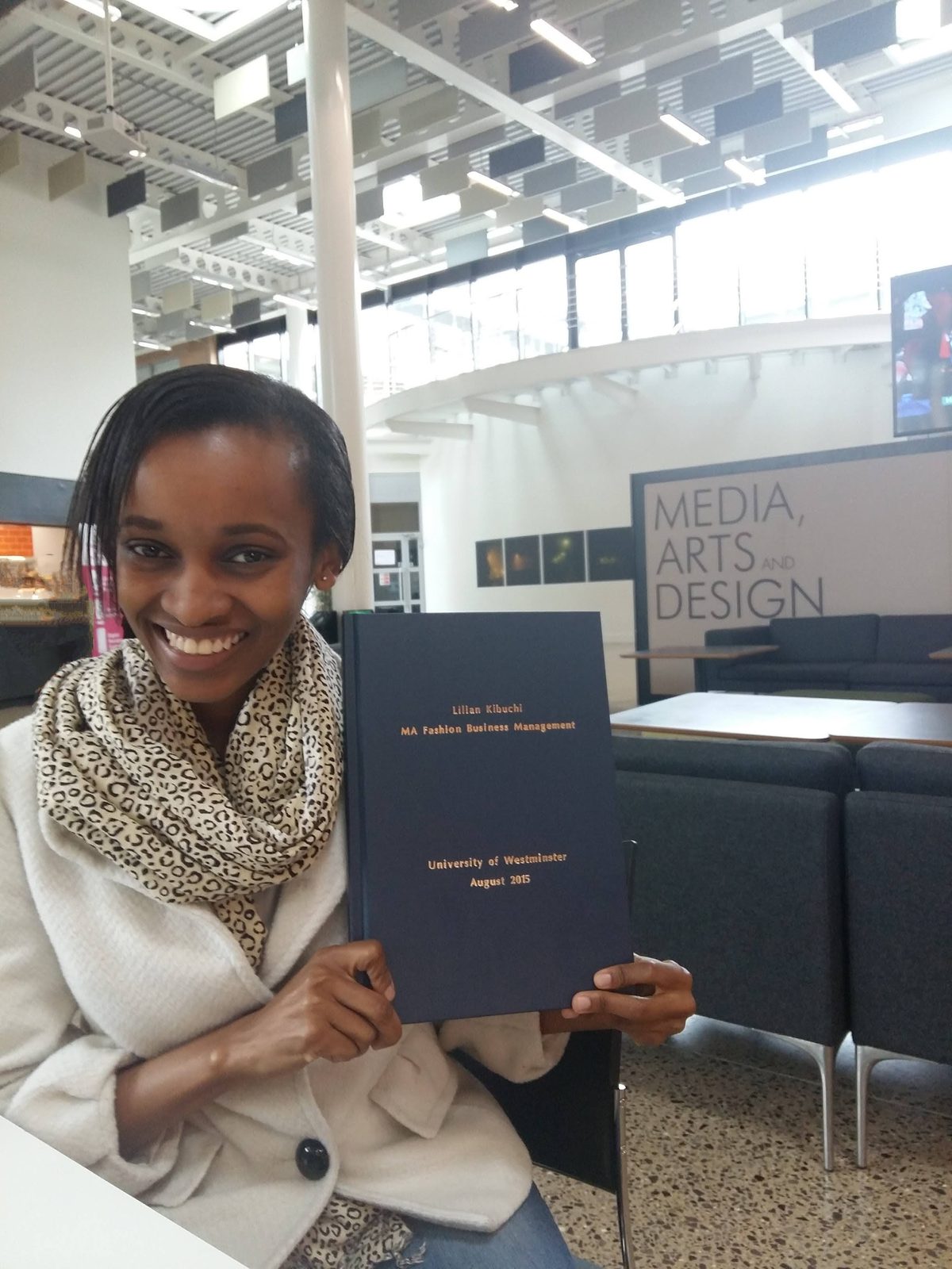 Holding a bound MA Fashion Business Management thesis in a university atrium.
